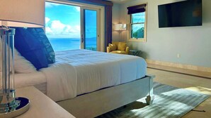 Una habitación de hotel con cama, una silla, televisión y vista al océano.