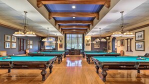 A pool hall with multiple pool tables, wooden floors, chandeliers, and framed pictures on the walls. - Indio Home w/ Private Pool & Community Amenities (Indio)