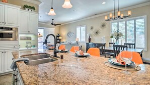 A spacious kitchen with granite countertops, white cabinets, and a dining area with orange chairs. - Indio Home w/ Private Pool & Community Amenities (Indio)