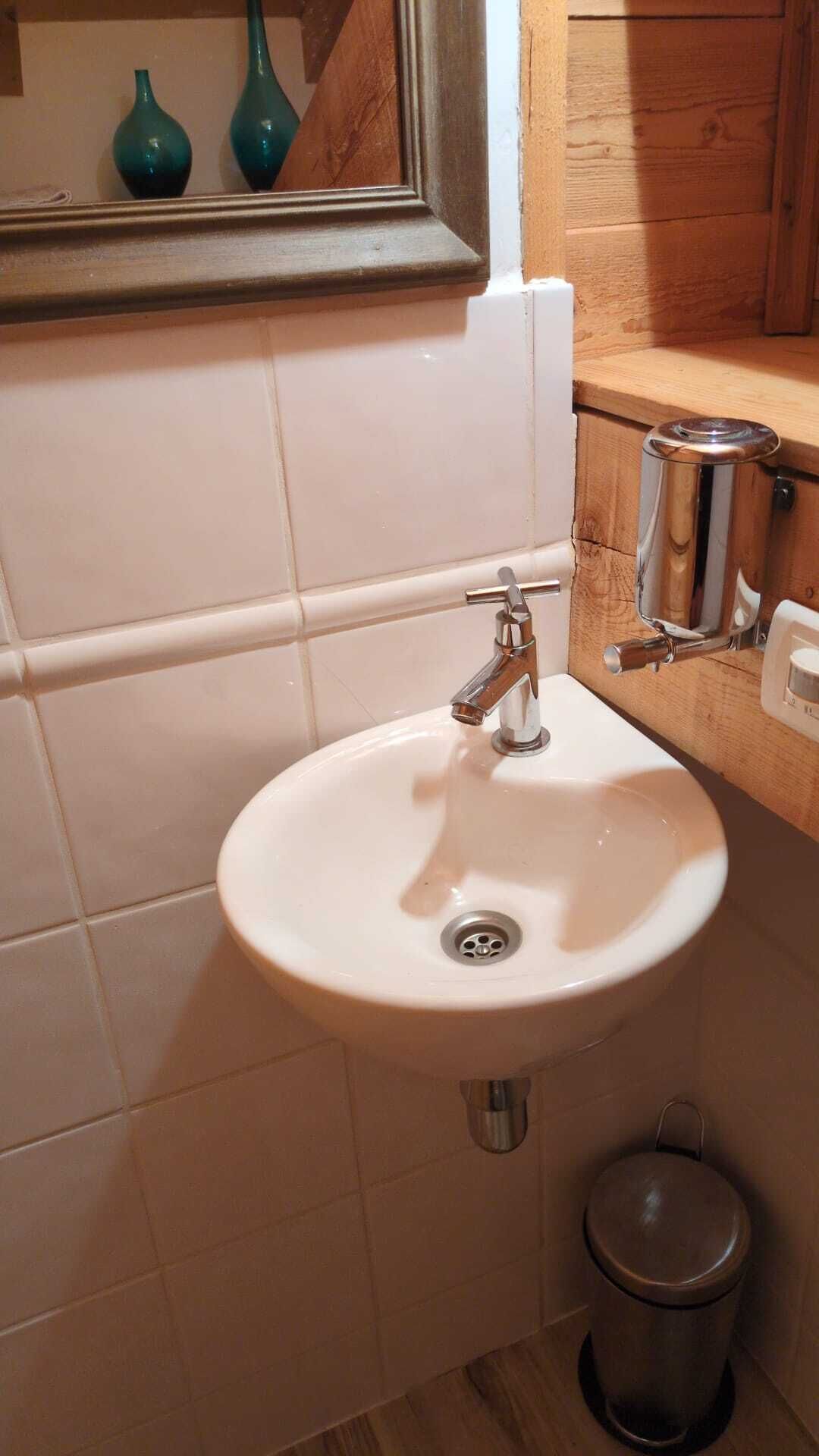 A bathroom with a white sink, chrome faucet, and a trash can.