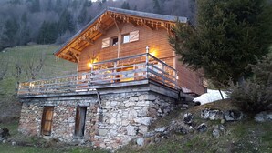 A wooden cabin with a stone foundation, a balcony with railings, and string lights.