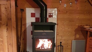 A cozy room with a wood-burning stove, two bean bags, wooden walls, and a rustic kitchen area.