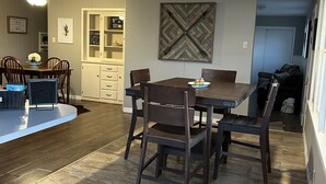 A dining area with a wooden table and chairs, a white cabinet, and a decorative wall piece.
