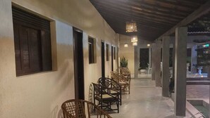 Uma área de estar coberta ao ar livre, com cadeiras de vime e um candeeiro pendente.