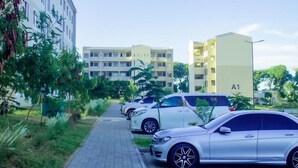 Fila de coches estacionados a lo largo de un camino pavimentado en una zona residencial con edificios altos y áreas verdes.