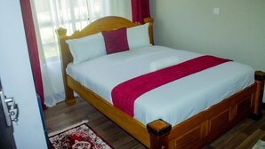 Una cama bien hecha con cabecera de madera, ropa de cama blanca y una manta roja.