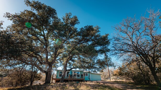A house surrounded by trees with a clear sky. - Enjoy our speakeasy at our 2 bedroom cottage! (Sunrise Beach Village)