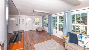A spacious living room with hardwood floors, a sofa with blue and white patterned cushions, a small side table, and a bench. - Enjoy our speakeasy at our 2 bedroom cottage! (Sunrise Beach Village)