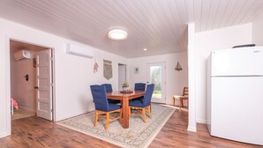 A dining area with a wooden table and blue chairs, a white refrigerator, and a patterned rug on a wooden floor. - Enjoy our speakeasy at our 2 bedroom cottage! (Sunrise Beach Village)