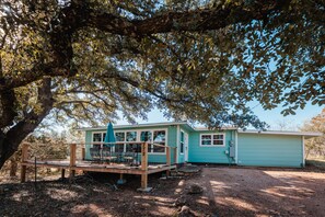 A turquoise house with a deck, a covered patio, and a fenced outdoor area. - Enjoy our speakeasy at our 2 bedroom cottage! (Sunrise Beach Village)