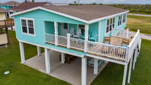 A turquoise house with a covered porch, white railings, and a small deck area.