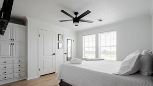 A bedroom with a bed, white wardrobe, ceiling fan, and large windows.