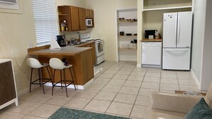 A compact kitchen with a central island, a microwave, an oven, and a refrigerator. There are two bar stools and a green rug on the floor.