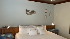 A bedroom with a bed, two bedside tables, a wall with decorative items, and a wooden ceiling.