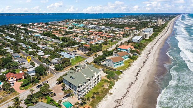 An aerial view of a coastal residential area with houses, a beach, and a marina.