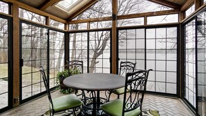 Een overdekt terras met een tafel en stoelen, grote ramen en een plafondventilator.
