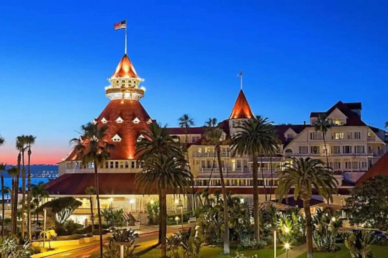 Un hotel gran de moltes plantes amb una torre destacada i una zona de jardí ben il·luminada.
