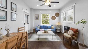 A living room with a blue sofa, wooden furniture, a ceiling fan, and framed artwork on the walls. - Unit 2 - B Ave Bungalows · Beachside 1/1, 5-10 Min Walk to Coronado Beach! (Coronado)
