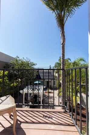 A balcony with a view of a house, a palm tree, and a chair.