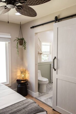 A bedroom with a bed, bedside table, hanging plant, and a ceiling fan.