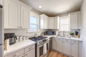 A modern kitchen with white cabinetry, a gas stove, a microwave, and a sink.