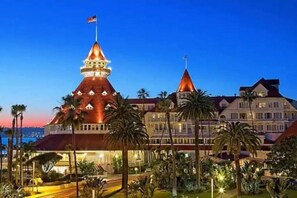 Un hotel grande e histórico con una torre destacada y múltiples agujas, rodeado de jardines cuidados y palmeras.