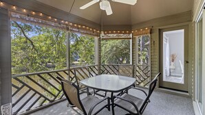 Um alpendre coberto com mesa e cadeiras, grandes janelas e ventilador de teto.