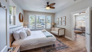 A spacious bedroom with a large bed, a ceiling fan, and a view of the outside through the windows.