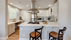 A modern kitchen with white cabinetry, a stainless steel range hood, and a central island with bar stools.