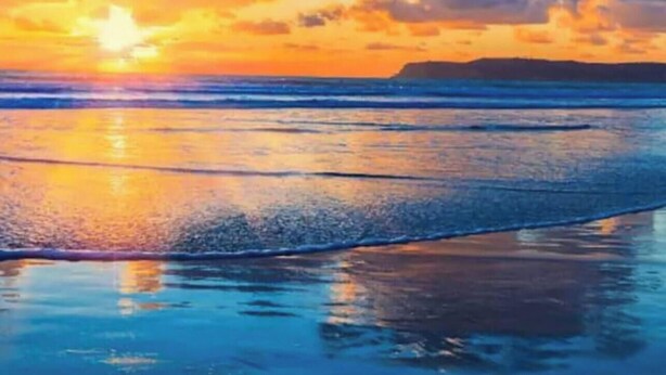 A beach with waves, a sunset, and a distant landmass.
