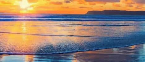A beach with a sunset, calm water, and a distant landmass.
