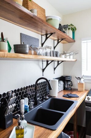 A kitchen with wooden shelves, a black faucet, a coffee machine, and a tiled backsplash. - Unit A - B Ave Bungalows · Cozy Beach Studio, 5 Min Walk to Coronado Beach! (Coronado)