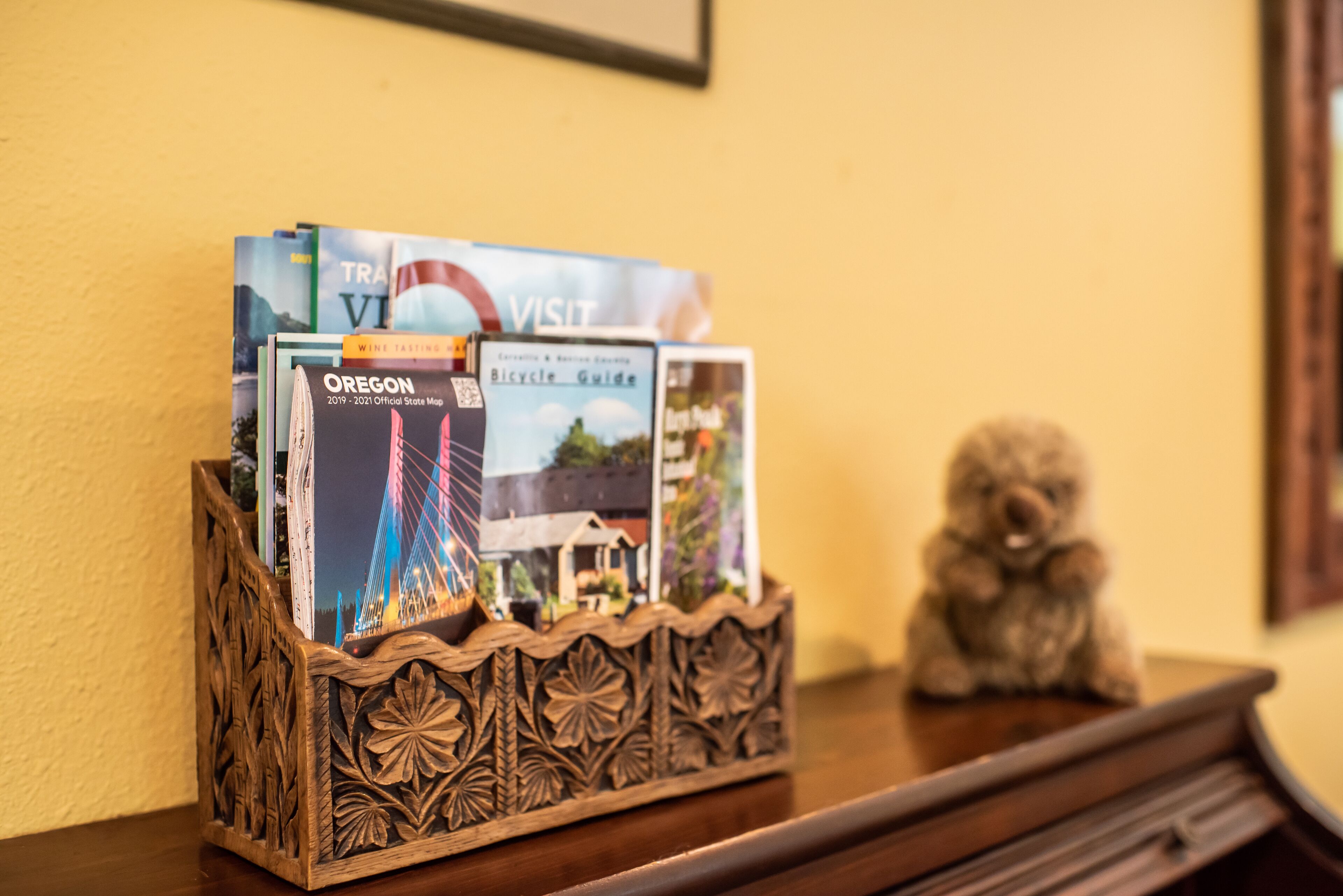 A wooden tray holding travel brochures and a small figurine on a wooden table.