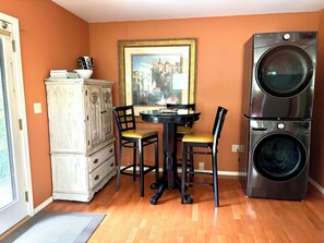 A compact kitchen with a dining table, chairs, a cabinet, and a stacked washer and dryer.