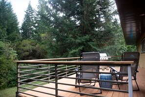 A wooden deck with metal railings, two chairs, a table, and a grill.