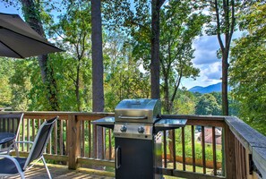 Una parrilla de barbacoa en una terraza de madera con vistas a árboles y montañas.