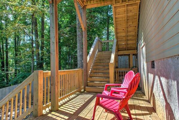 A wooden deck with a staircase leading to a covered area, surrounded by trees.