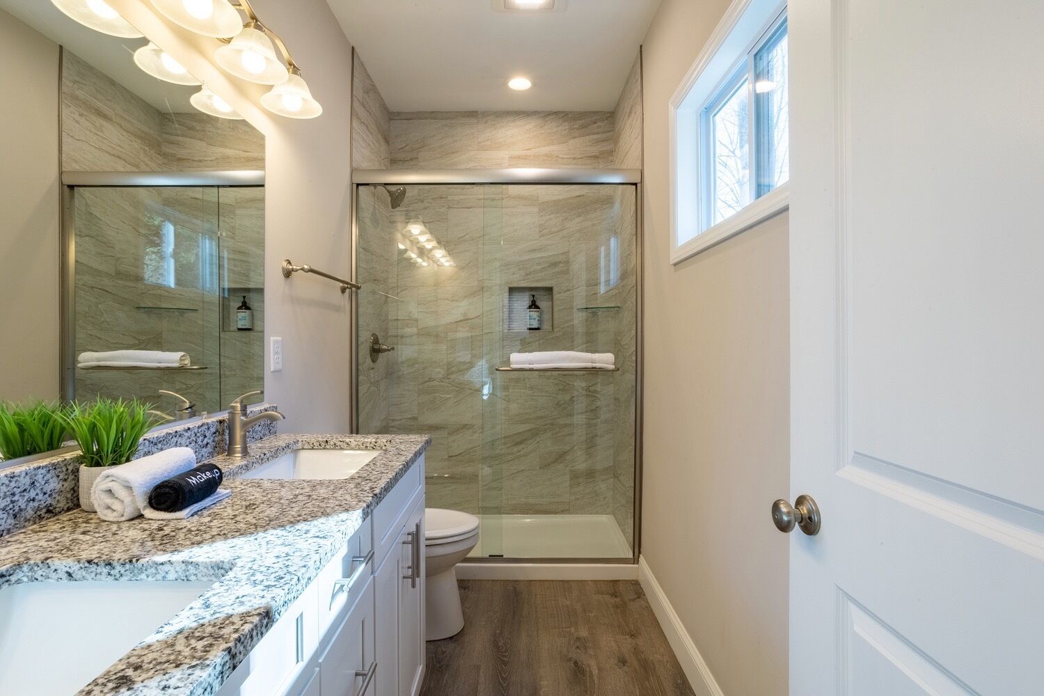 Un baño moderno con ducha de vidrio, tocador de granito y un espejo grande.