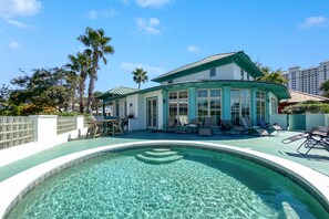 A pool area with a clear blue pool, lounge chairs, and a building with large windows and a green roof.