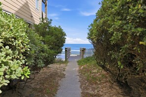 A pathway leading to a beach with a wooden fence and dense foliage on either side.