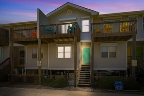A two-story residential building with a central staircase, balconies, and a green door. - Not quite ocean front, but almost! Just a few steps to the sand! Pet friendly. (Surf City)