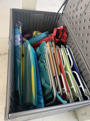 A storage bin containing various items including a blue and yellow bag, a red bag, and several metal tools. - Not quite ocean front, but almost! Just a few steps to the sand! Pet friendly. (Surf City)