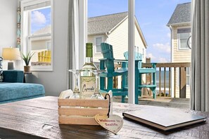 A wooden crate with a glass bottle and a heart-shaped sign on a wooden table, with a view of a house and chairs outside.