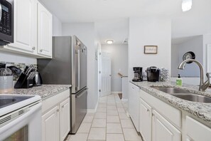A modern kitchen with white cabinets, a stainless steel refrigerator, a built-in oven, and a granite countertop. - Not quite ocean front, but almost! Just a few steps to the sand! Pet friendly. (Surf City)