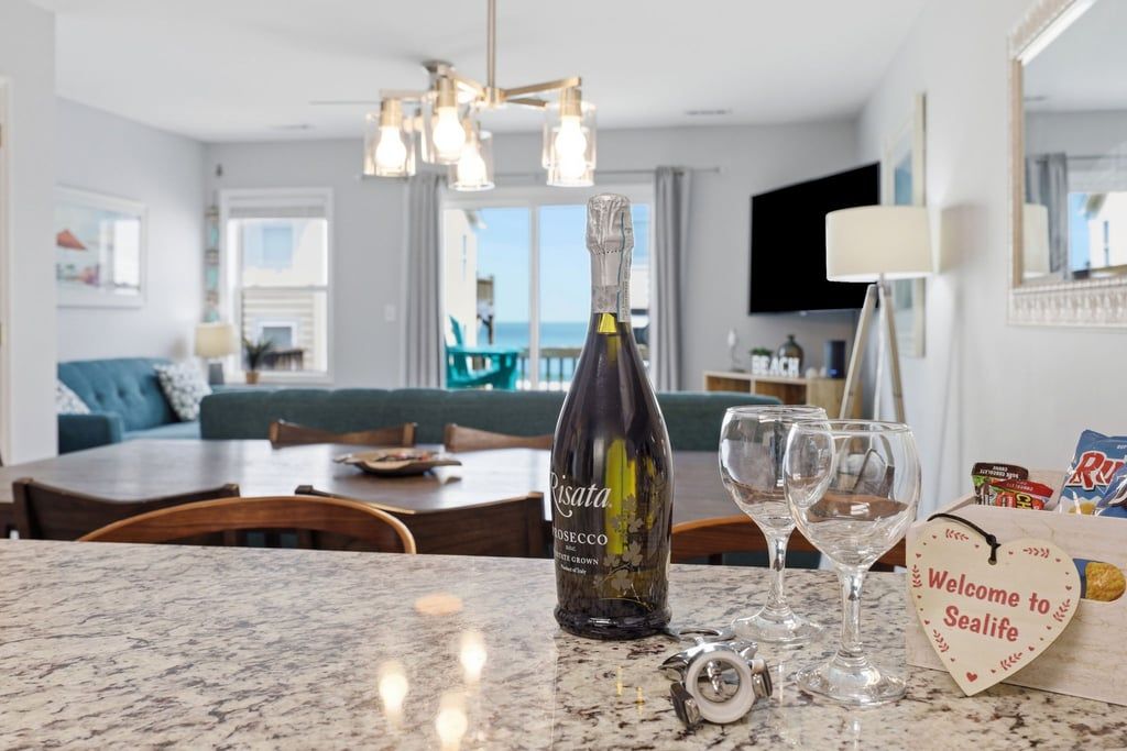A bottle of wine, empty glasses, and a welcome sign on a table in a room with a view.