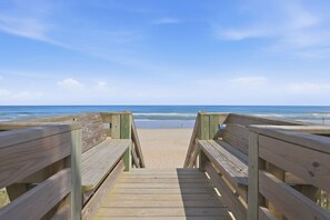 A wooden boardwalk leading to a sandy beach with a clear blue sky.