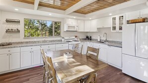 Una cocina moderna con armarios blancos, encimera de granito y comedor con mesa y sillas de madera.