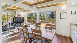 Un salón amplio con una gran mesa de madera y sillas, una chimenea de piedra, y un balcón con vistas a árboles.