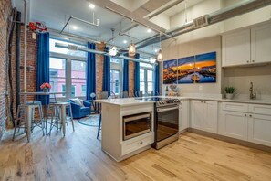 A modern kitchen with a central island, white cabinetry, and a large window with blue curtains.