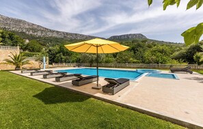 Relax by the pool surrounded by lush greenery and a scenic backdrop of rocky hills.
